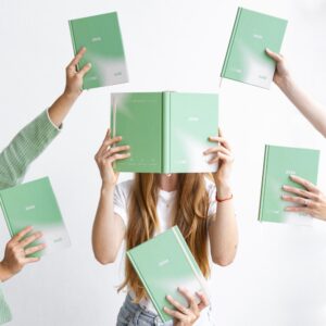 Skupina lidí drží zelené diáře s rokem 2026, zatímco si zakrývají obličeje.