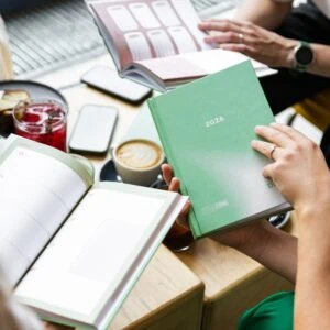 Rok 2026 na obálce plánovače, otevřené stránky s prázdnými políčky, káva a nápoje na stole.