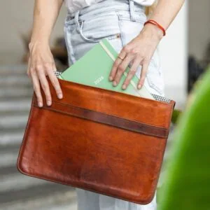 Žena drží koženou tašku s plánem na rok 2026 a zápisníkem, nachází se v moderním prostředí.