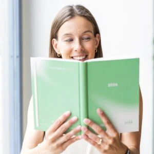 Žena se usmívá a drží otevřený zelený diář na rok 2026.