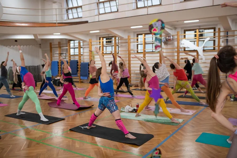 Skupina žen cvičí na podložkách v sále, provádějí různé pohyby a protahování.