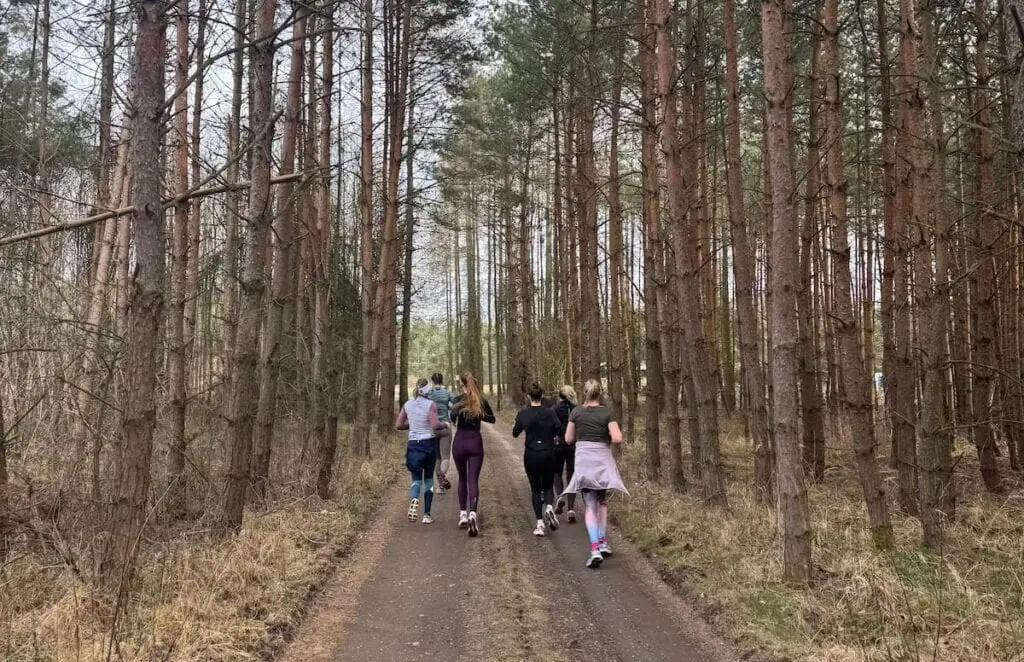 Skupina běžců trénuje na lesní cestě obklopené stromy.