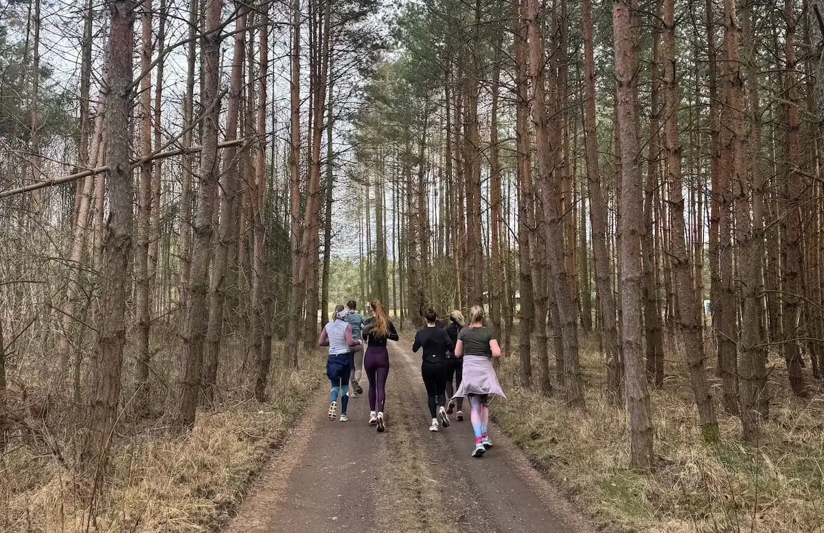 Skupina běžců trénuje na lesní cestě obklopené stromy.