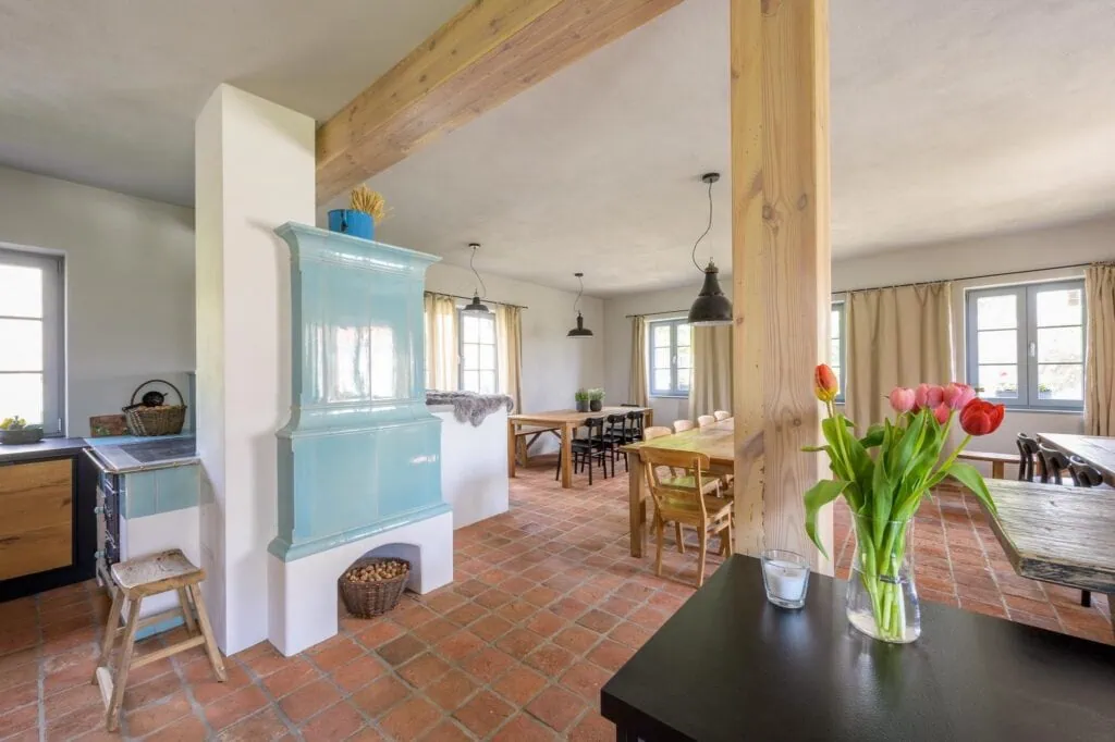 Moderní interiér s modro-bílým sporákem, dřevěnými stoly a květinami na stole. Světlé místnosti s okny.