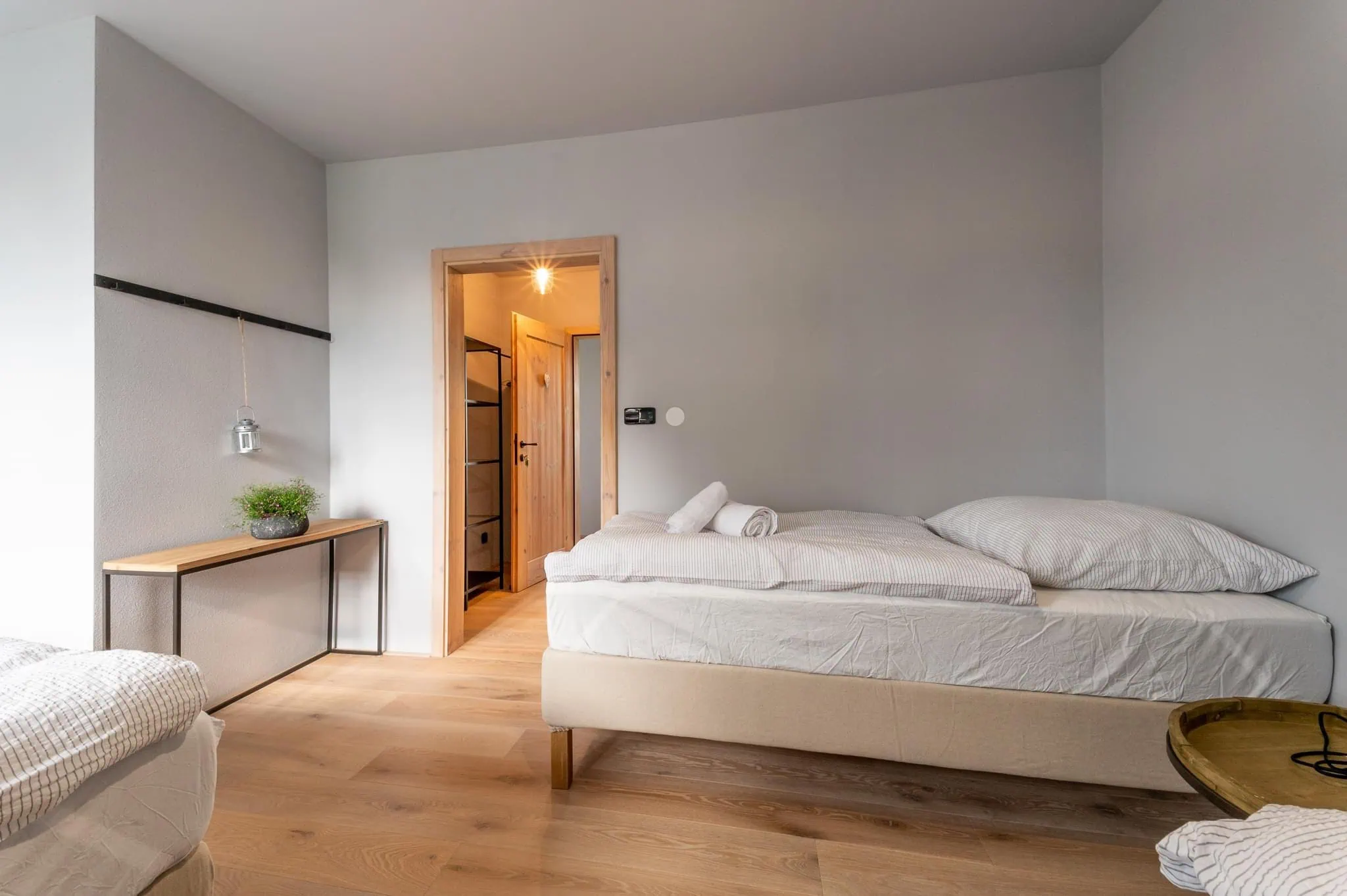 Moderní pokoj s dvěma postelemi, dřevěným nábytkem a dveřmi vedoucími do další místnosti.