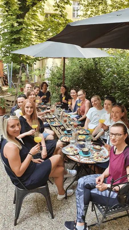 Skupina žen sedí u stolu na zahradě, drží sklenice s nápoji a vychutnávají si jídlo.